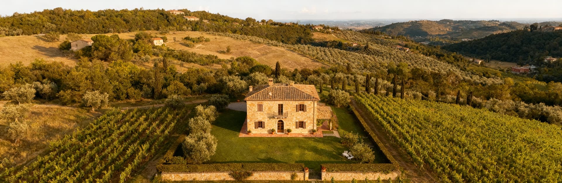 Villa storica in pietra immersa nel paesaggio toscano del Chianti, circondata da vigneti e uliveti, cielo sereno.