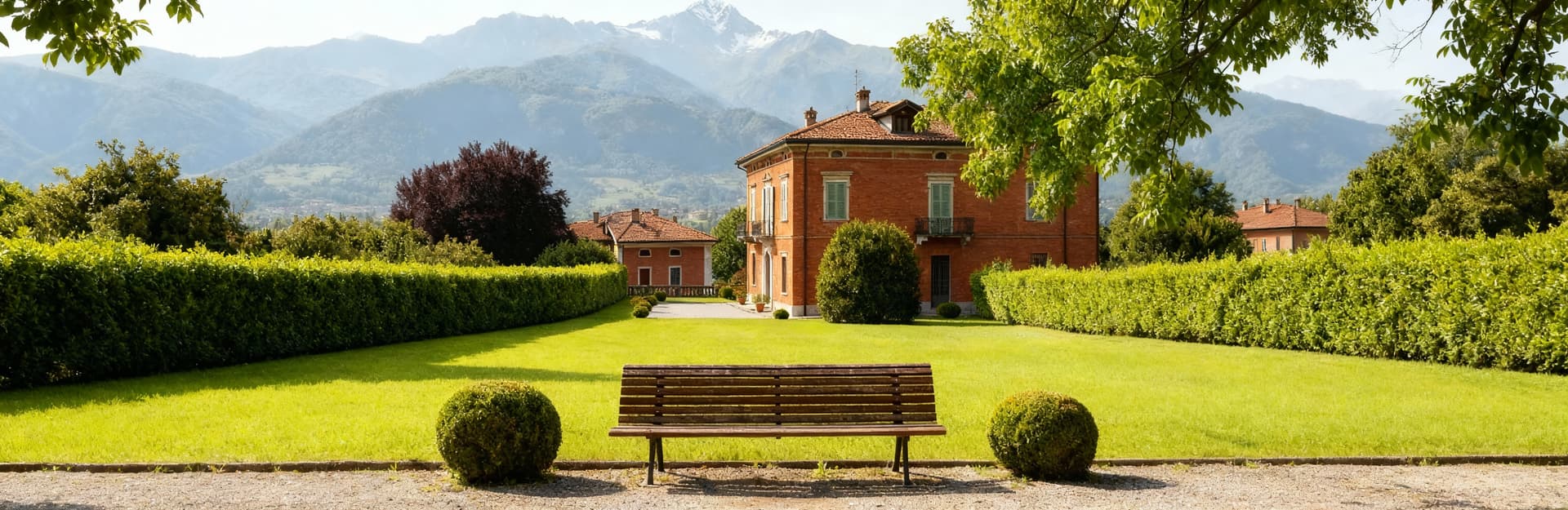 Immobili di prestigio a Cuneo, eleganti ville circondate da giardini verdi e panorama alpino nel cielo sereno.