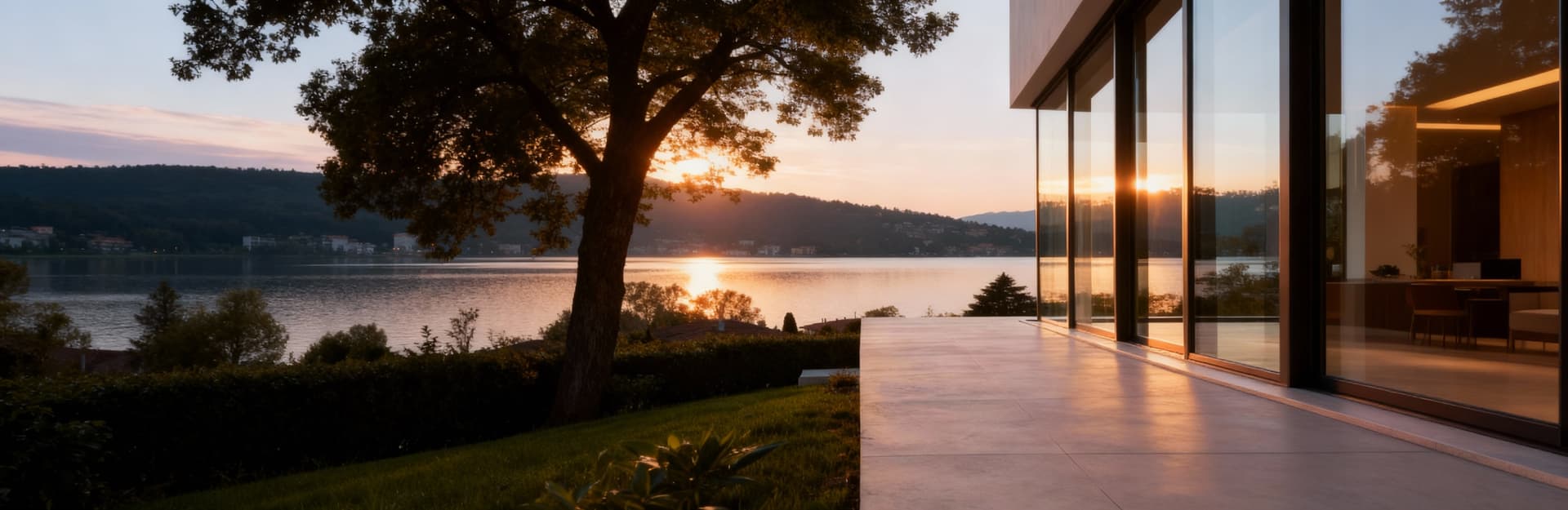 Attico di lusso a Varese con vista lago, ampie vetrate e atmosfera calda al tramonto, realizzato in vetro e intonaco chiaro.