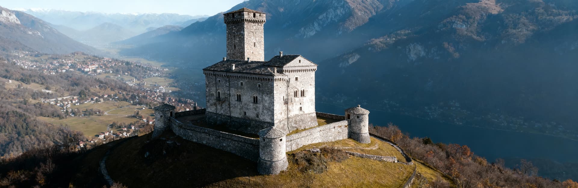 Castello storico su collina nel Verbano-Cusio-Ossola, circondato da montagne, con pareti in pietra grigia e cielo sereno.