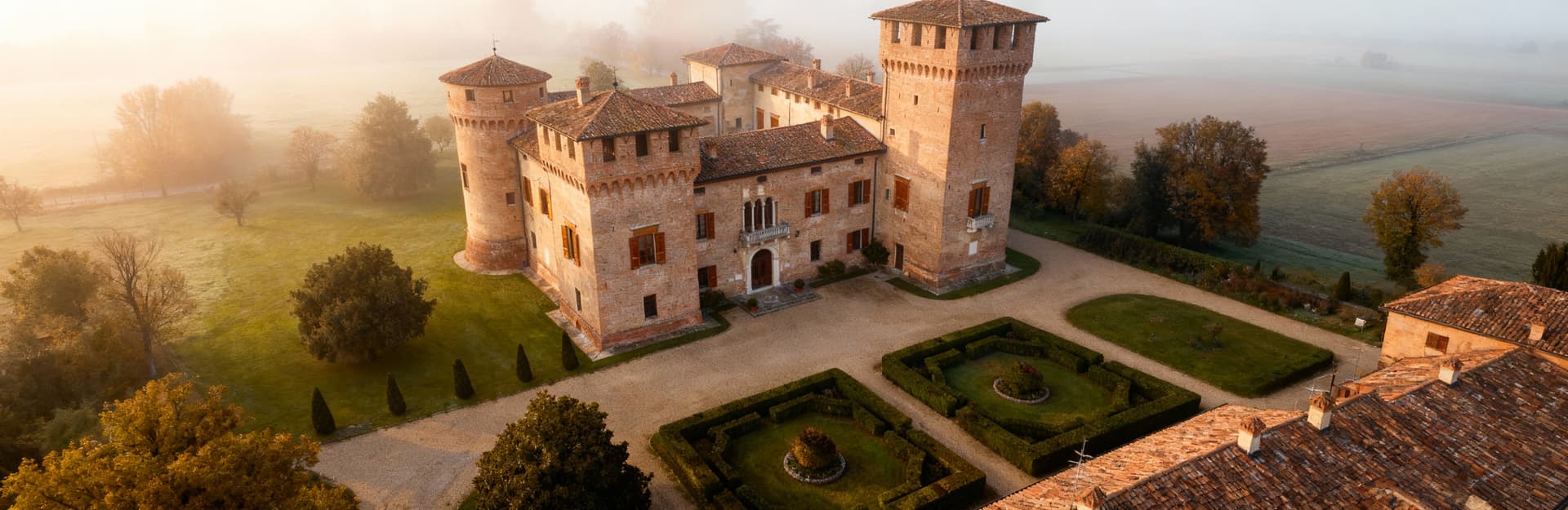 Castello storico a Lodi con giardino lussureggiante, avvolto da nebbia mattutina, esempio di architettura di lusso.