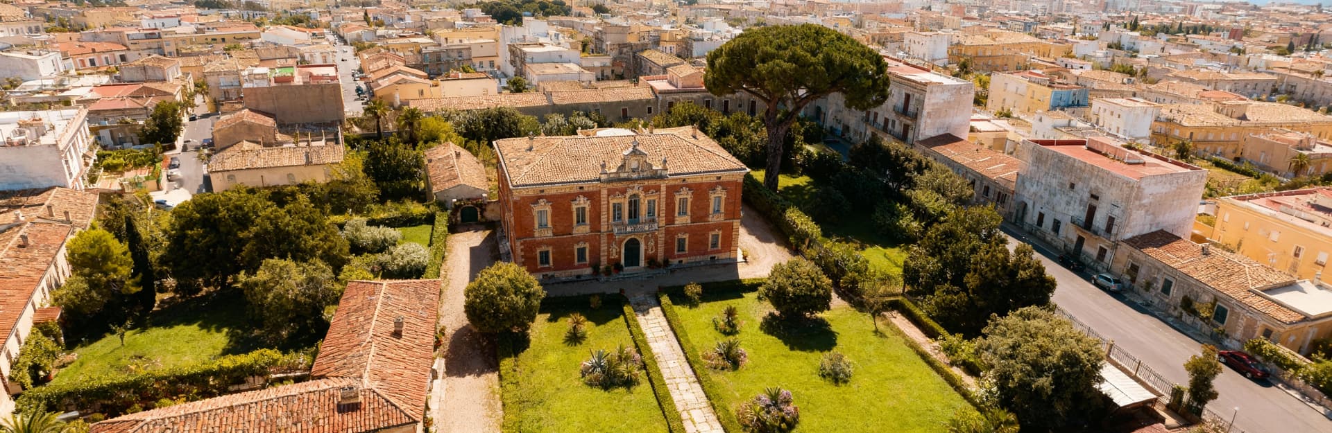 Villa storica a Sassari con architettura barocca, giardino curato e vista aerea sul contesto urbano circostante.