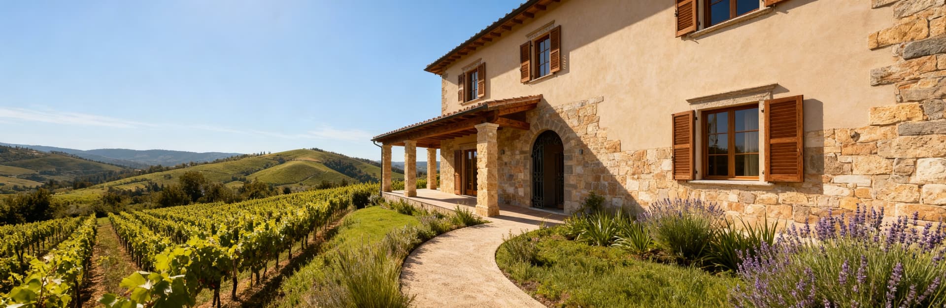 Elegante villa in pietra e legno a Pistoia, circondata da vigneti e colline, sotto un cielo azzurro e sole splendente.