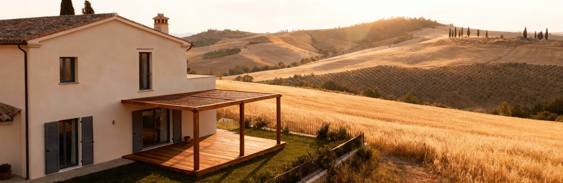 Villa esclusiva in Val d'Orcia, circondata da colline e campi dorati, con facciate chiare e terrazze in legno, nella luce del pomeriggio.