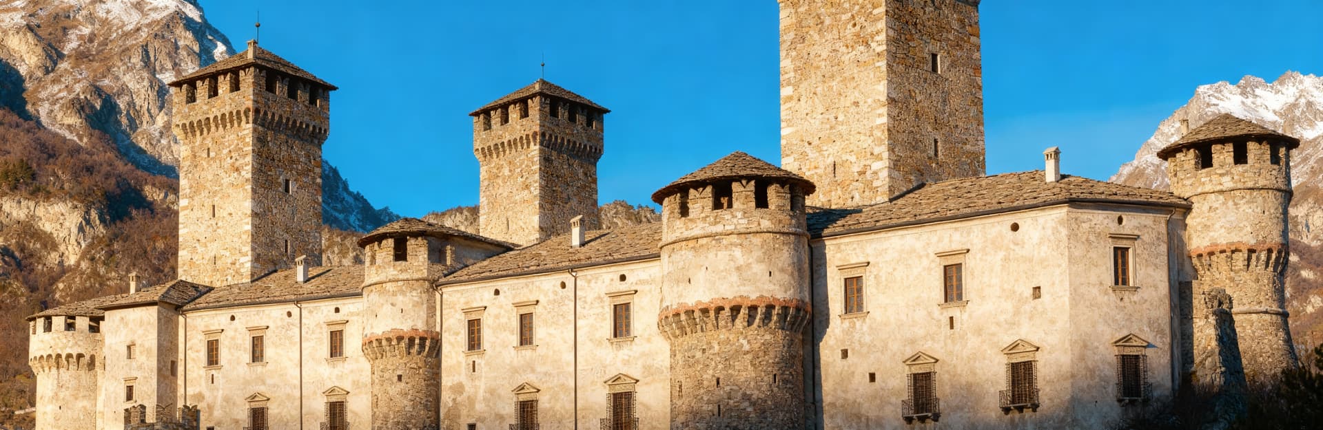 Castello prestigioso ad Aosta, circondato dalle Alpi, con torri storiche e luce mattutina che illumina il paesaggio.
