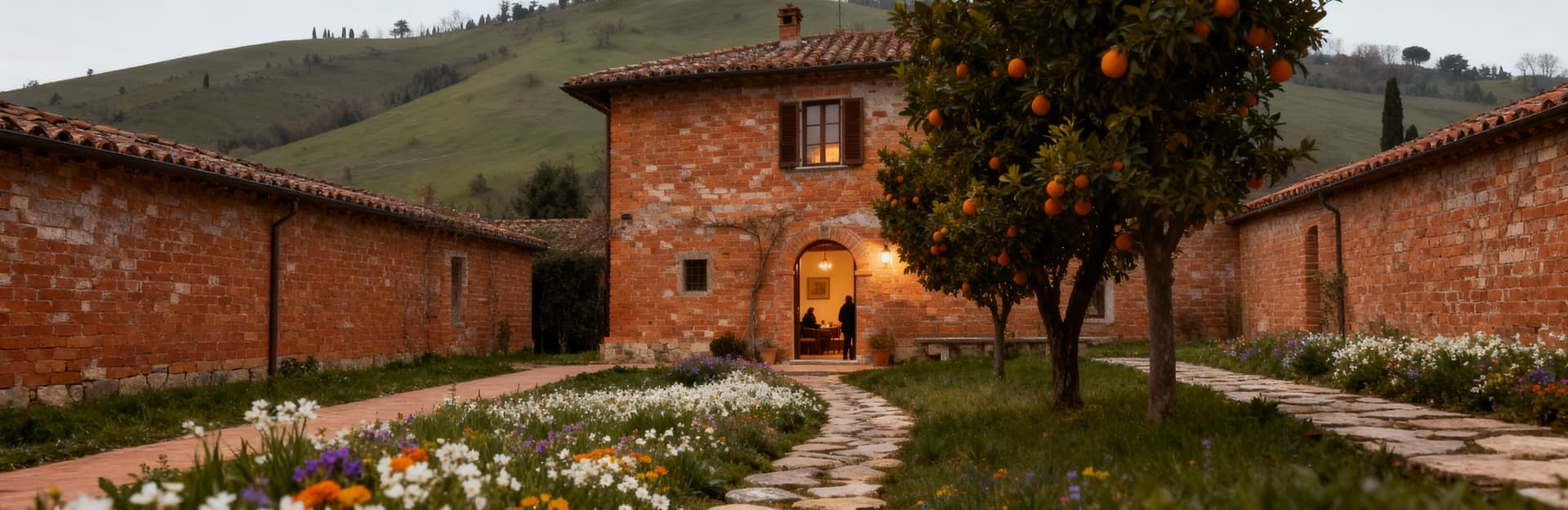 Agriturismo rustico in Piemonte, circondato da colline verdi, con sentiero di pietre e fiori, in una luce invernale calda.