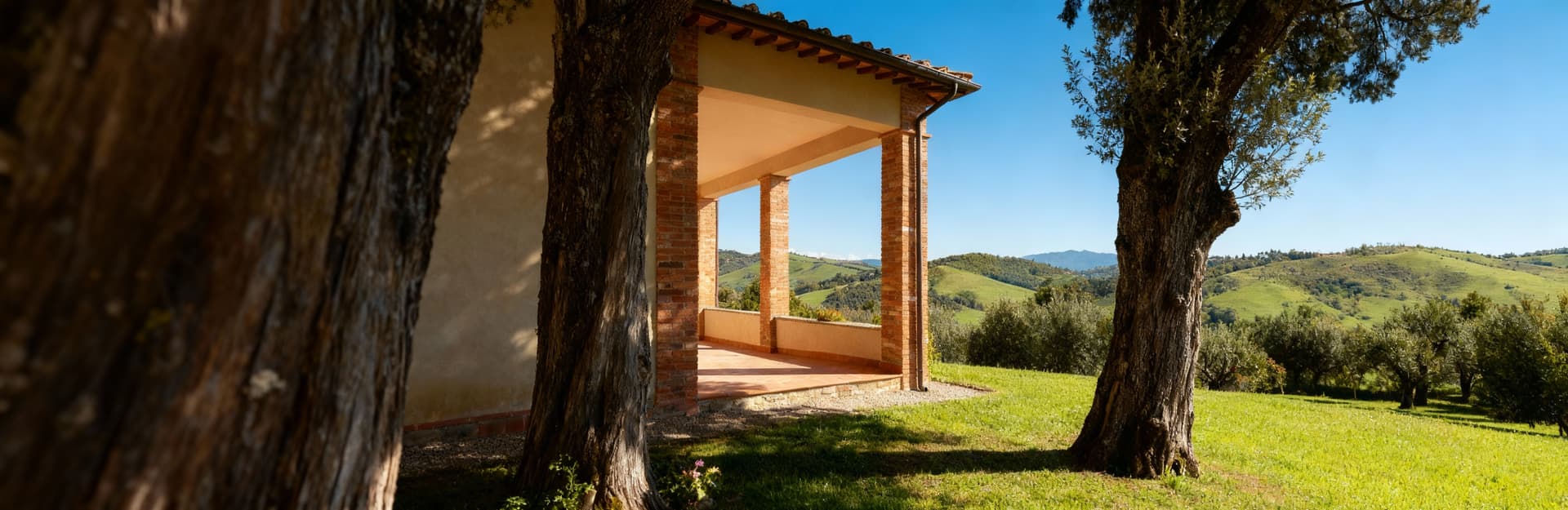 Colonica in vendita ad Arezzo: pareti in mattoni, portico ampio e vista sulle colline verdi, circondata da alberi secolari.