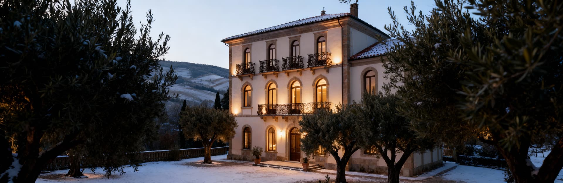 Elegante palazzo toscano con balconi in ferro battuto, circondato da ulivi e colline, illuminato da luce invernale.