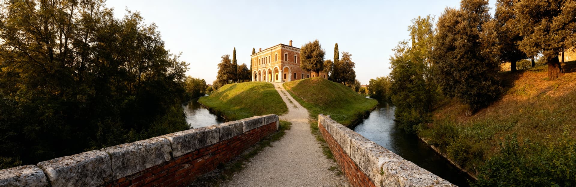 Villa storica a Treviso, mattoni a vista e archi in pietra, immersa in un paesaggio collinare illuminato dal sole.