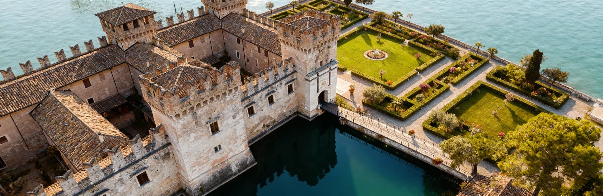 Castello storico in pietra affacciato su un lago in Veneto, circondato da un giardino all'italiana e con riflessi sul'acqua.