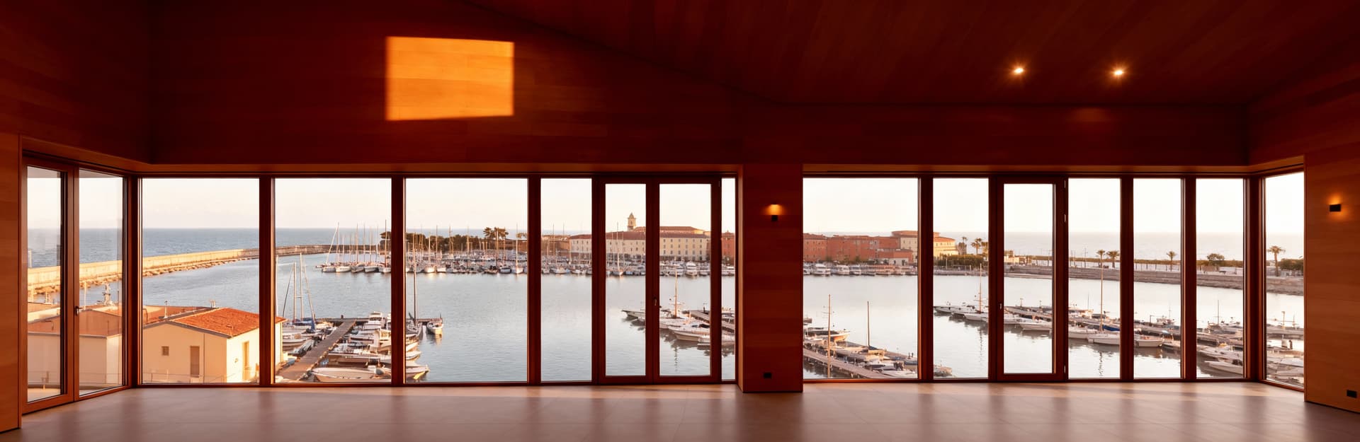 Attico moderno a Livorno con ampie vetrate sul porto, arredi in legno naturale e luce pomeridiana che riscalda l'ambiente.