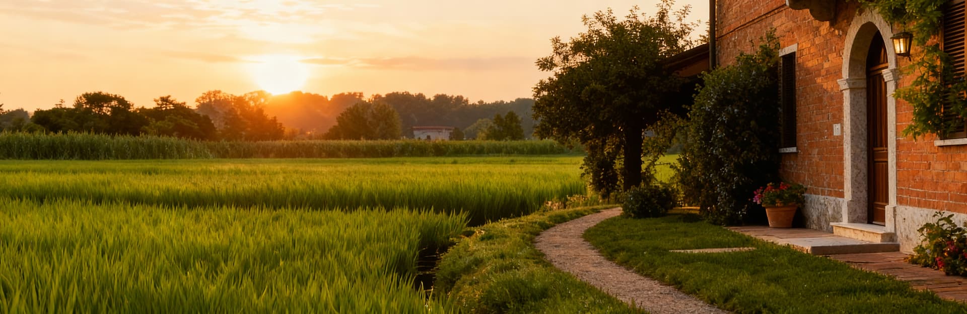 Casale in mattoni a Novara, circondato da risaie verdi e tramonto, evocando atmosfere piemontesi e tranquillità naturale.