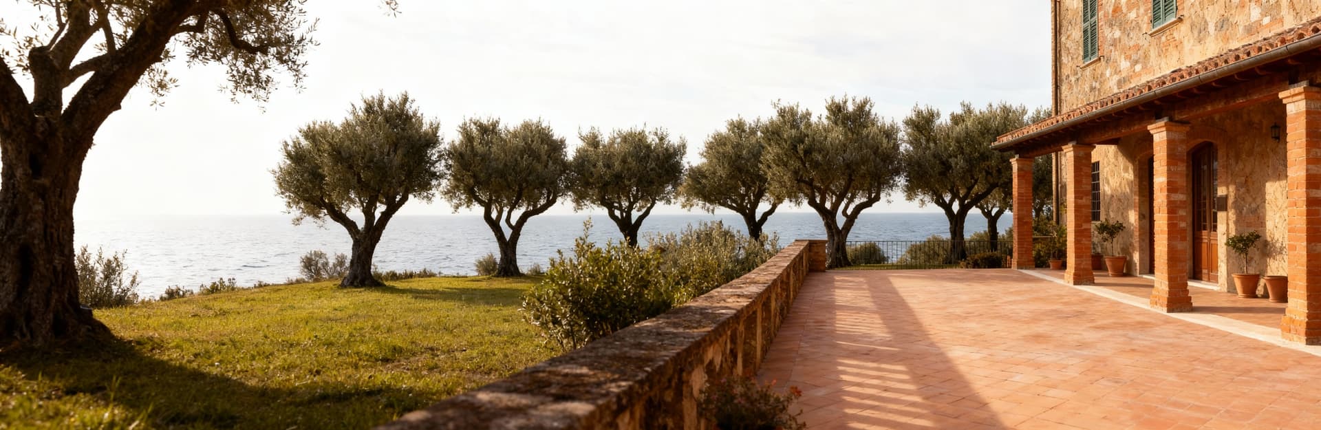 Rustico toscano con terrazza panoramica su uliveti, facciata in cotto e luce invernale, atmosfera calda e tranquilla.