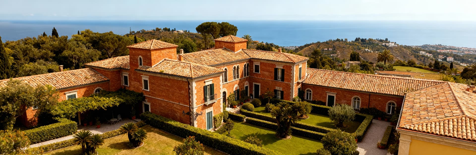 Albergo storico in Campania con facciate in mattoni, circondato da giardini, vista sul mare e colline sotto un cielo nuvoloso.