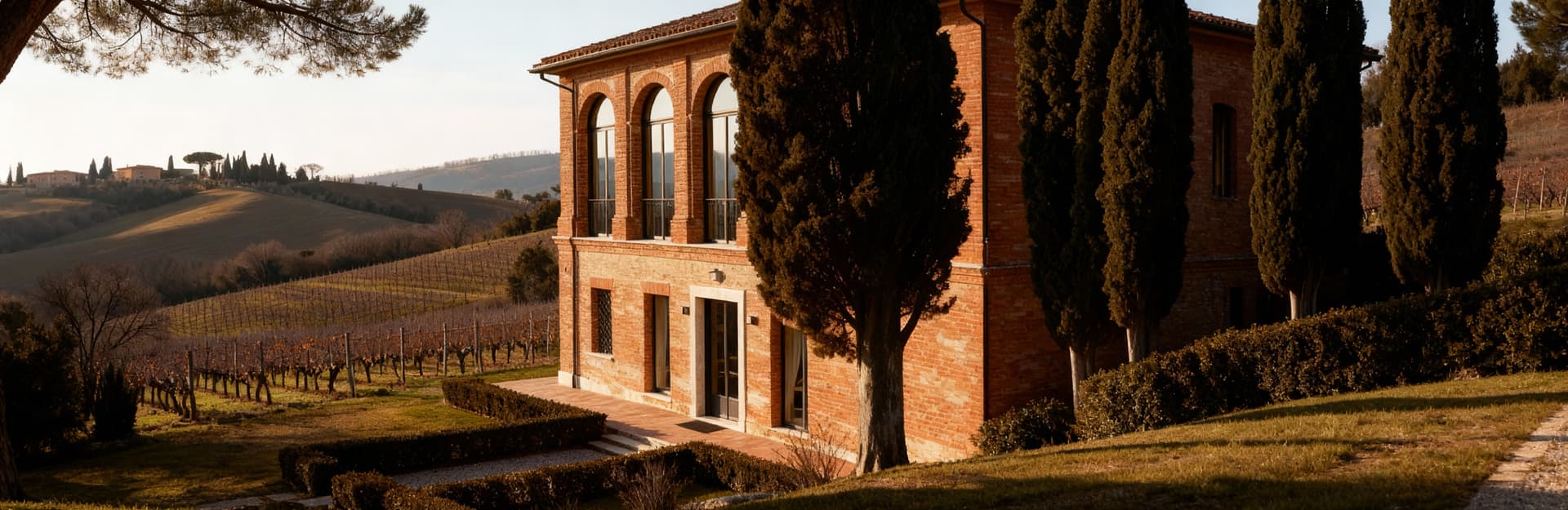 Villa storica a Fermo tra dolci colline, con facciate in mattoni e ampie vetrate, circondata da alberi e vigne.