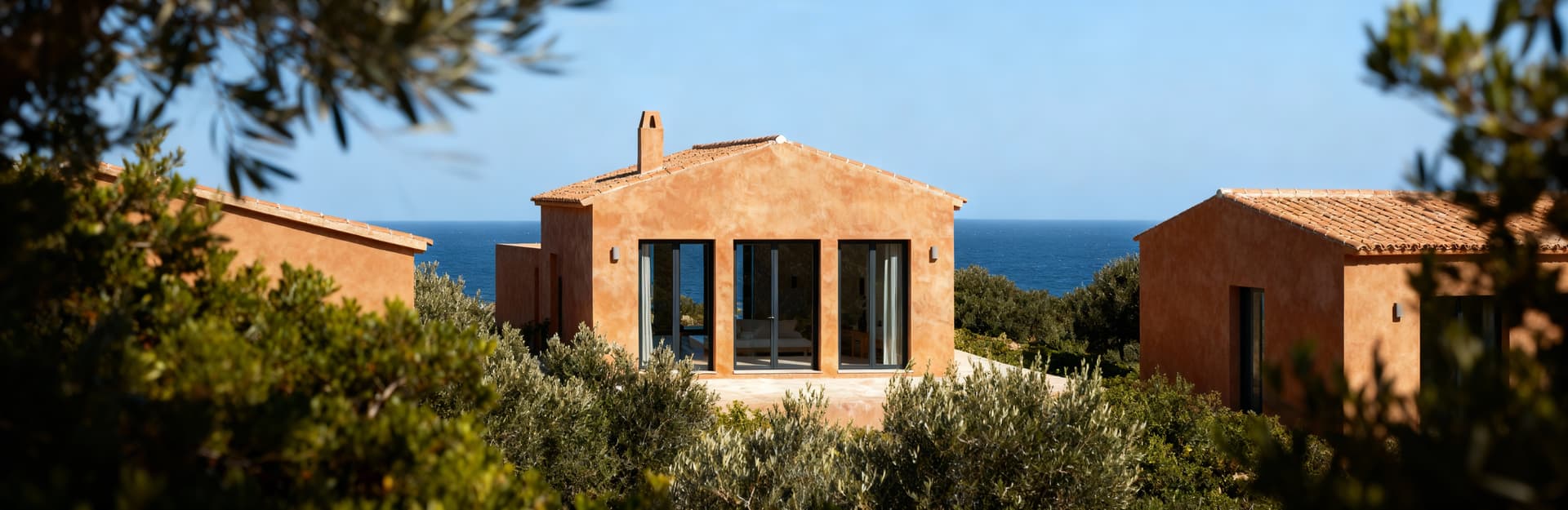 Villa di lusso affacciata sul mare nella Provincia del Sud Sardegna, con facciata in cotto e grandi vetrate, cielo sereno.