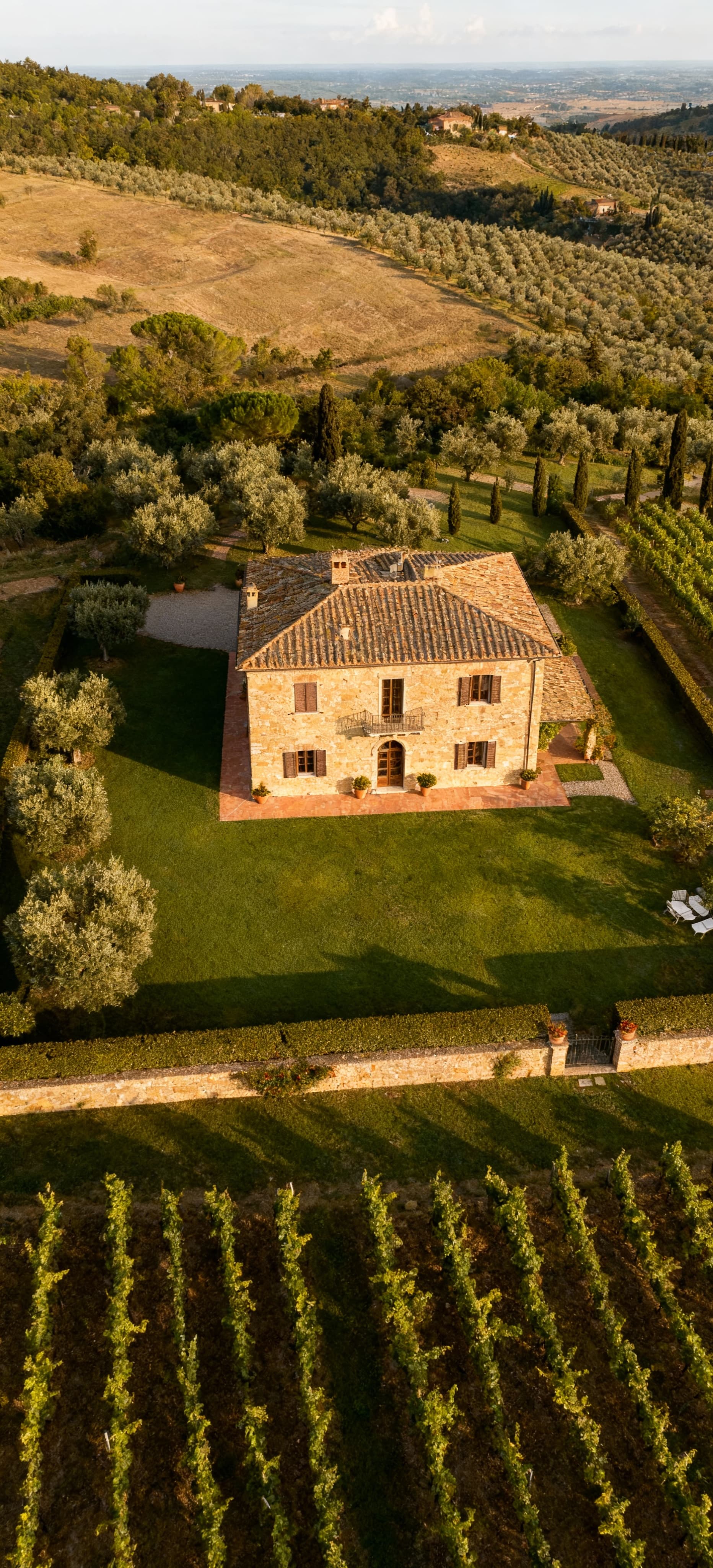Villa storica in pietra immersa nel paesaggio toscano del Chianti, circondata da vigneti e uliveti, cielo sereno.
