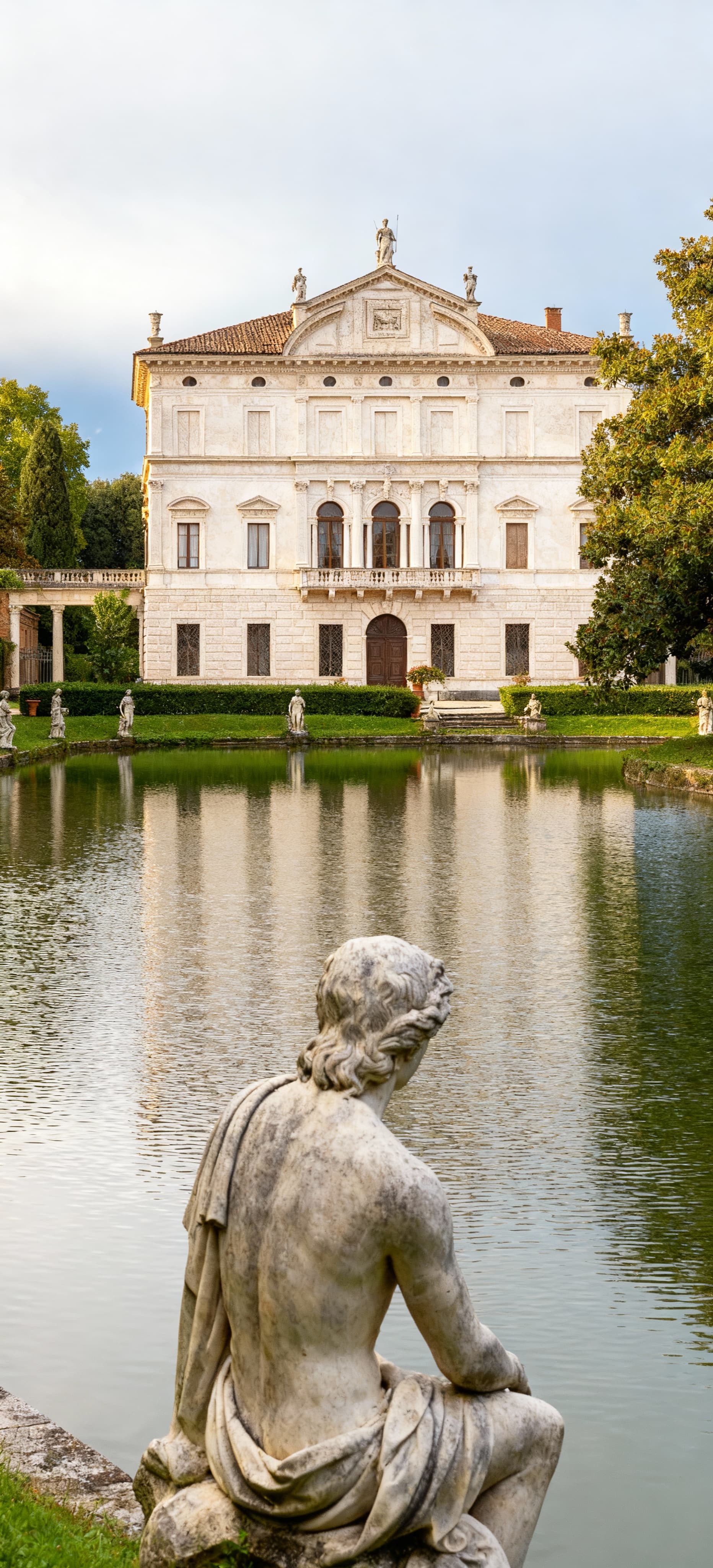 Villa storica a Mantova con facciata in pietra chiara, giardini lussureggianti e lago sereno in un contesto di lusso.