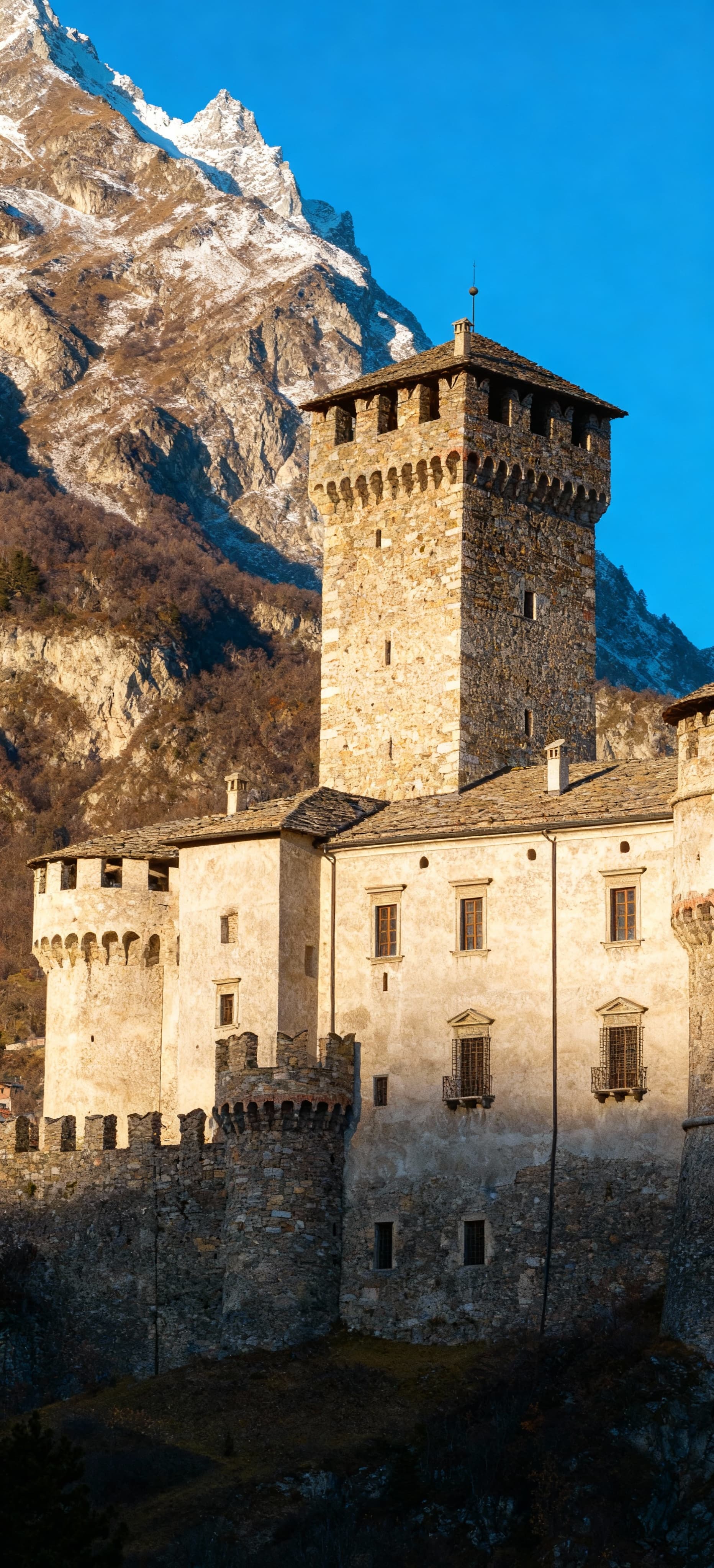 Castello prestigioso ad Aosta, circondato dalle Alpi, con torri storiche e luce mattutina che illumina il paesaggio.