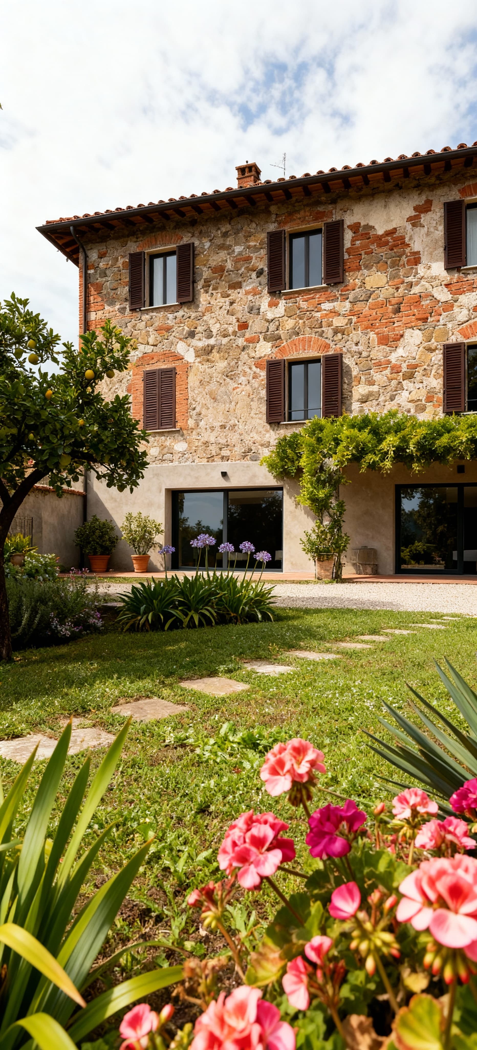 Rustico ristrutturato a Lucca, circondato da un giardino rigoglioso, mix di elementi antichi e moderni. Dettagli vivaci di piante e fiori.
