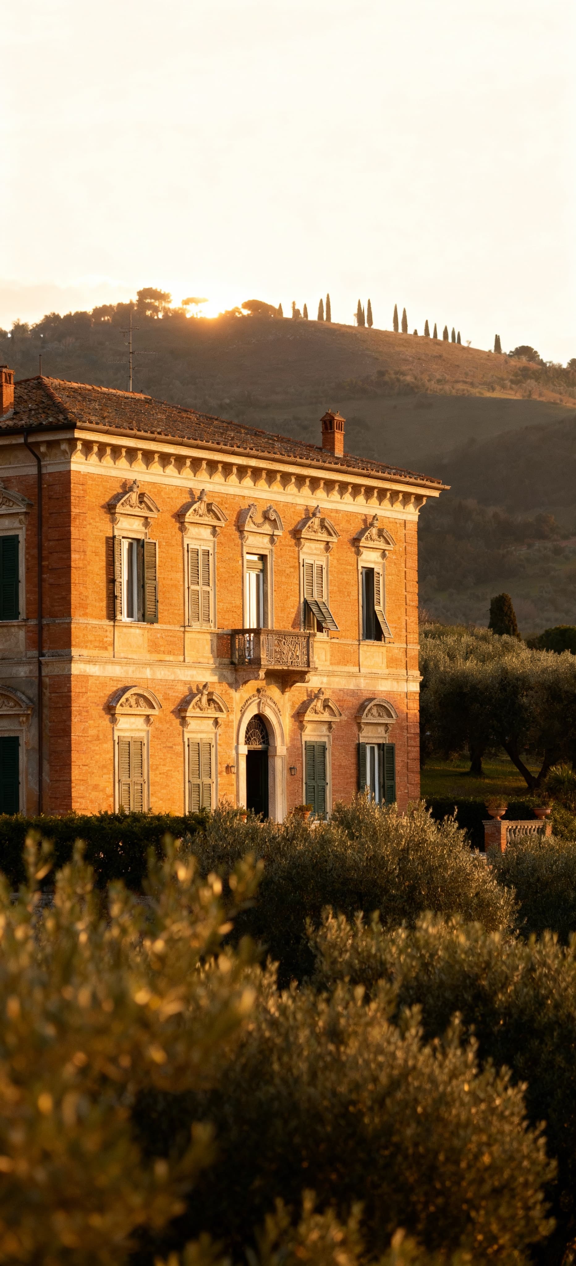 Vista di una storica villa a Lucca, in Toscana, circondata da uliveti e colline, illuminata dalla luce mattutina.