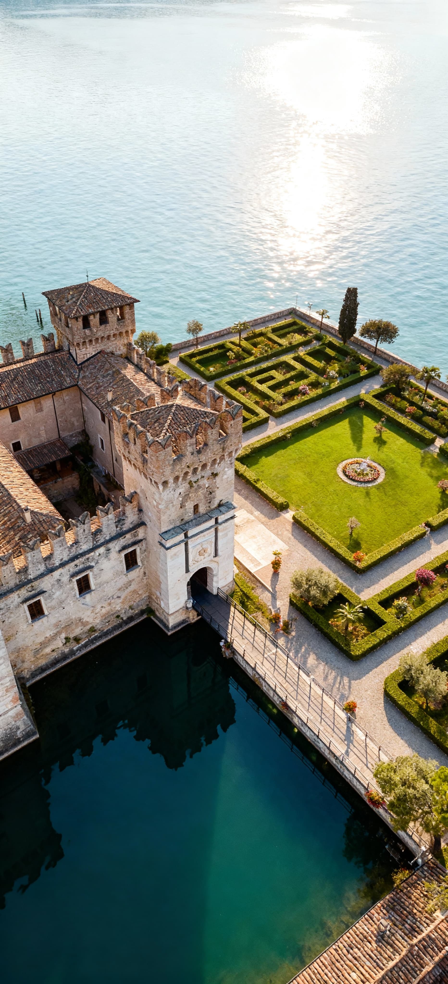 Castello storico in pietra affacciato su un lago in Veneto, circondato da un giardino all'italiana e con riflessi sul'acqua.