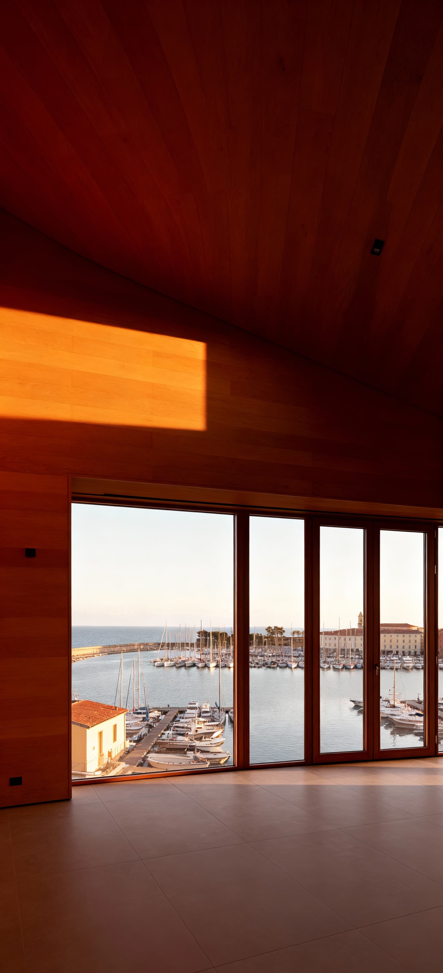 Attico moderno a Livorno con ampie vetrate sul porto, arredi in legno naturale e luce pomeridiana che riscalda l'ambiente.