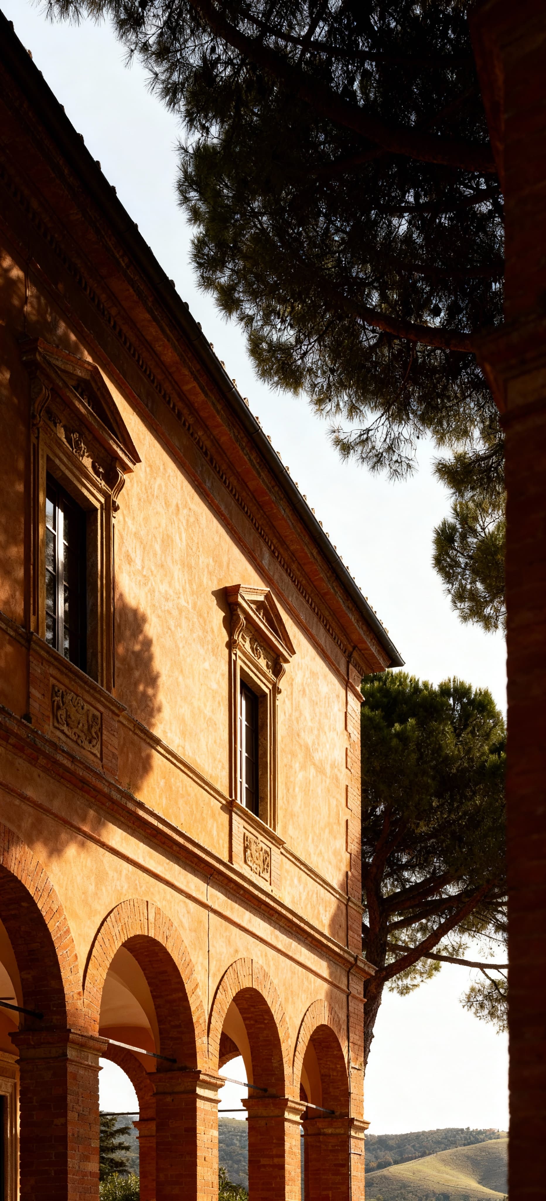 Palazzo storico a Grosseto, illuminato dal sole, con eleganti archi e finestre ornate, circondato da pini marittimi e colline toscane.