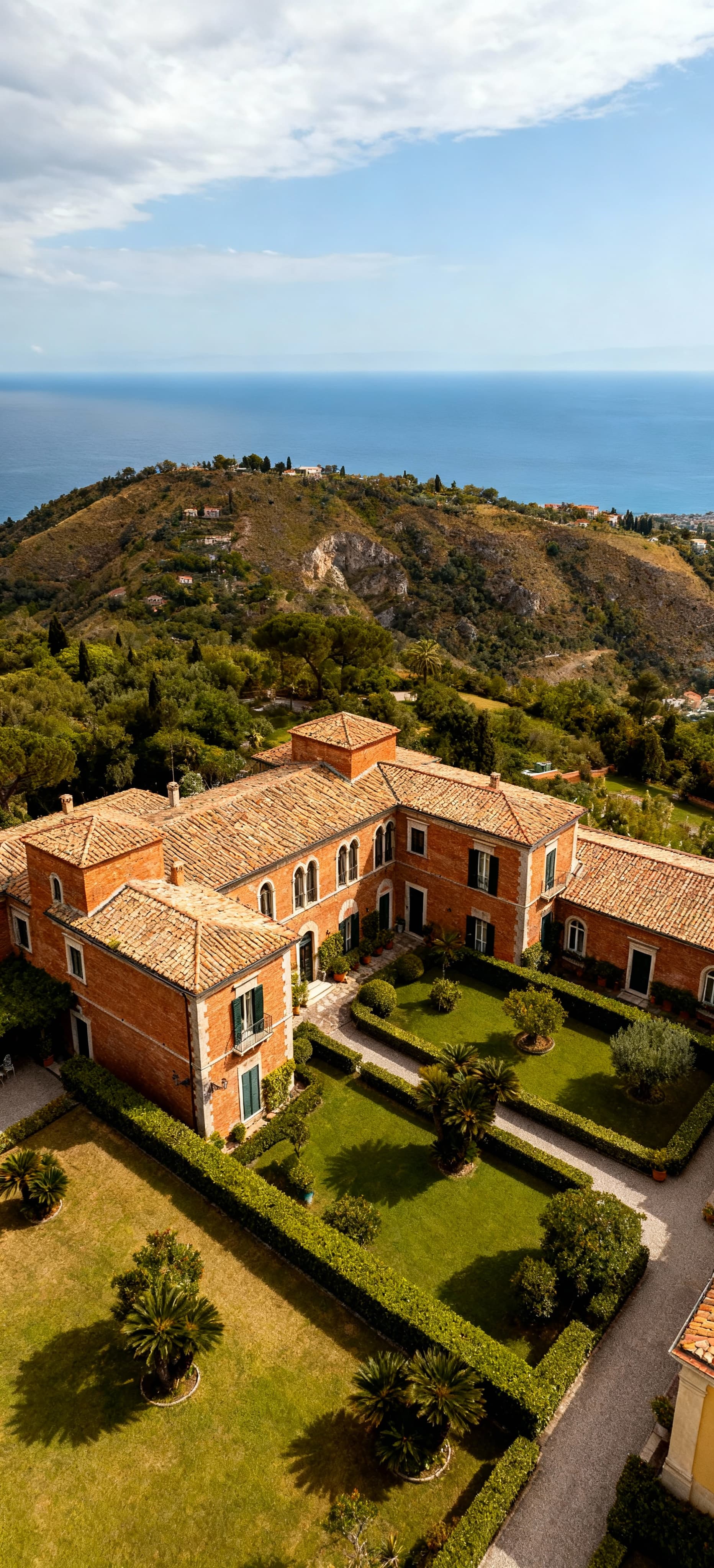 Albergo storico in Campania con facciate in mattoni, circondato da giardini, vista sul mare e colline sotto un cielo nuvoloso.