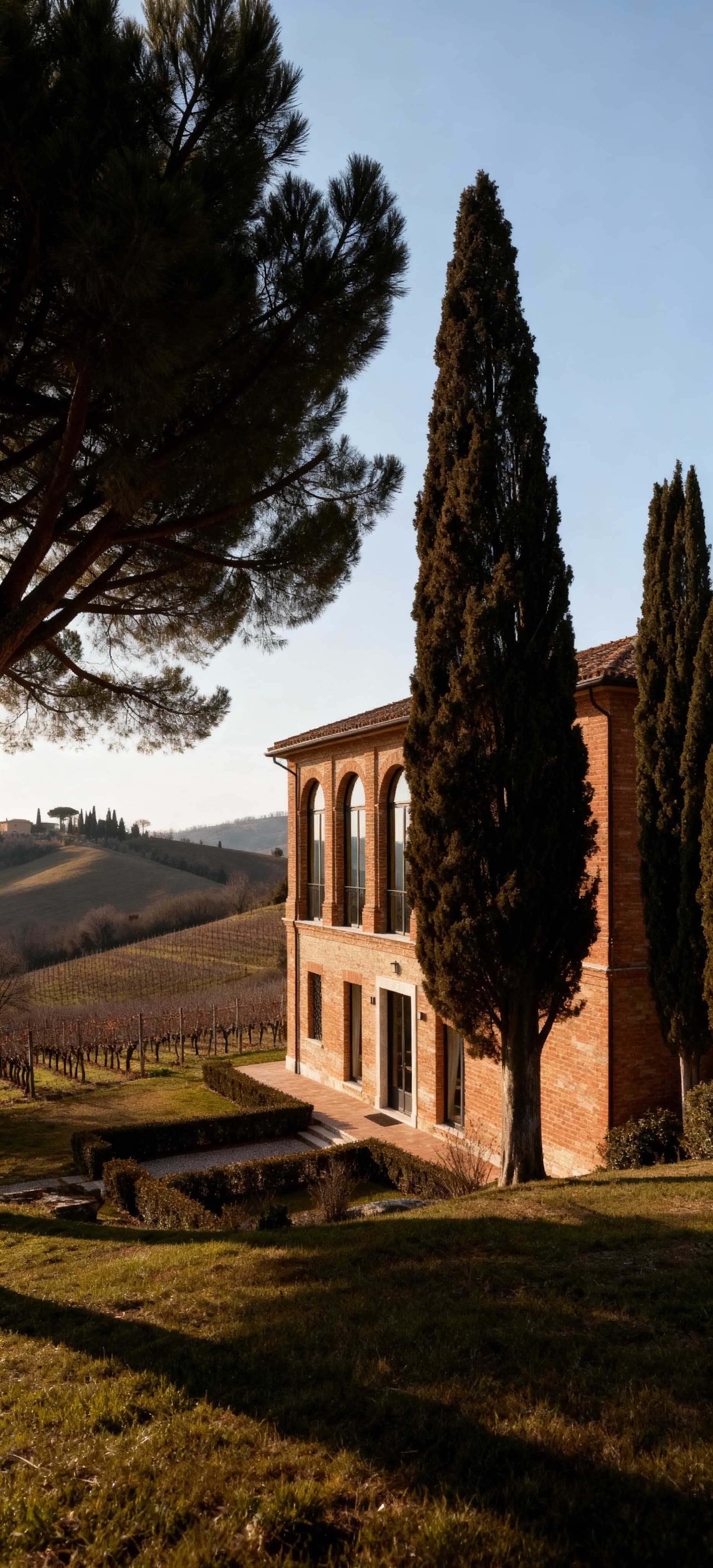 Villa storica a Fermo tra dolci colline, con facciate in mattoni e ampie vetrate, circondata da alberi e vigne.