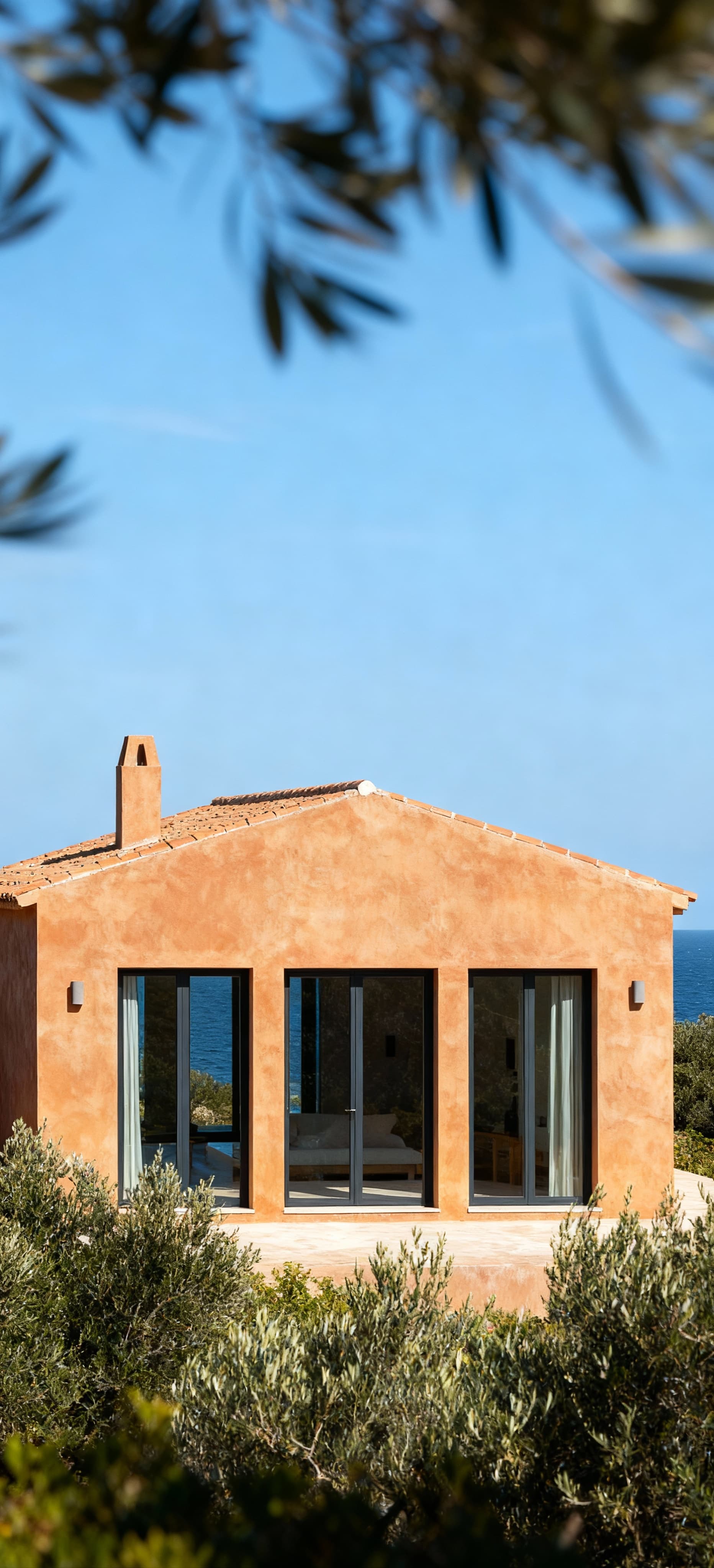 Villa di lusso affacciata sul mare nella Provincia del Sud Sardegna, con facciata in cotto e grandi vetrate, cielo sereno.