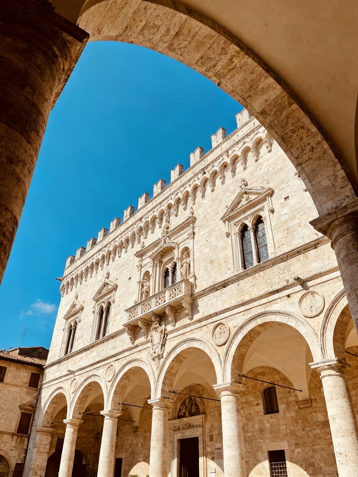 Historic building in Perugia with stone arches and ornate facade, showcasing architectural grandeur against a clear blue sky.