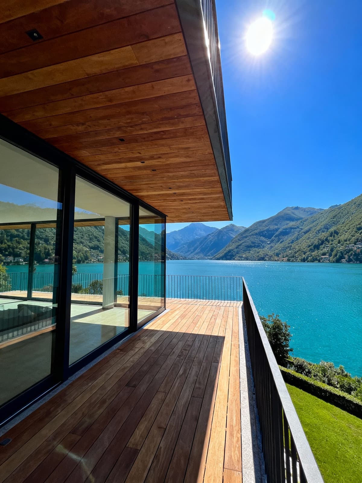 Exclusive penthouses overlooking the turquoise waters of Lake Como, featuring wooden and glass terraces, set against the Alps.