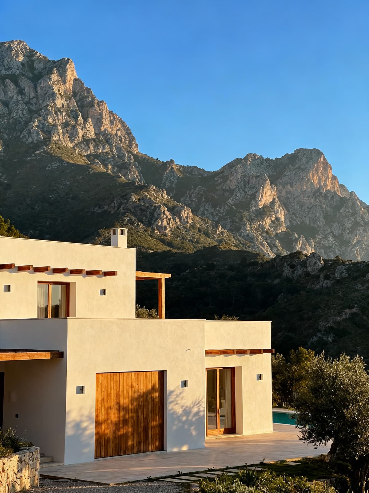 Luxury villa nestled among the majestic Sicilian mountains, showcasing a light stucco façade and natural wood details.