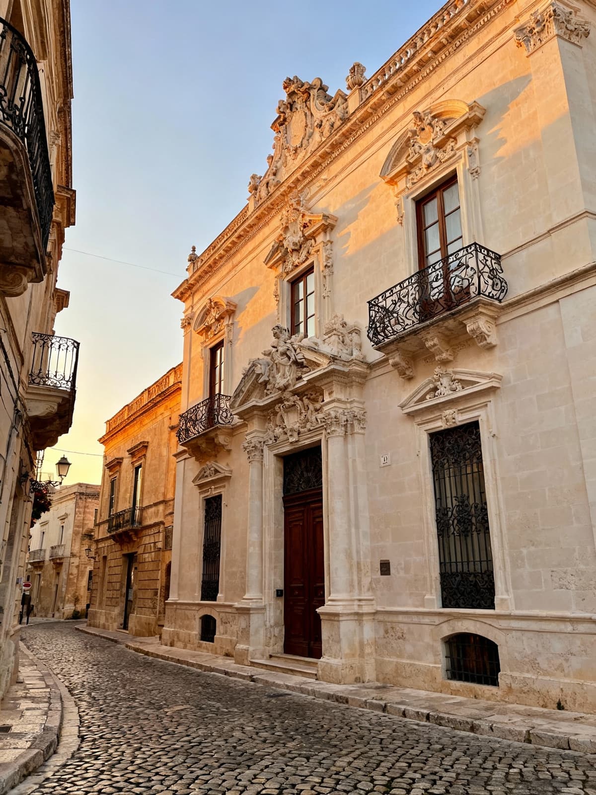 Palazzi nobiliari barocchi a Lecce, con facciate eleganti su strade acciottolate illuminate dalla luce del tardo pomeriggio.