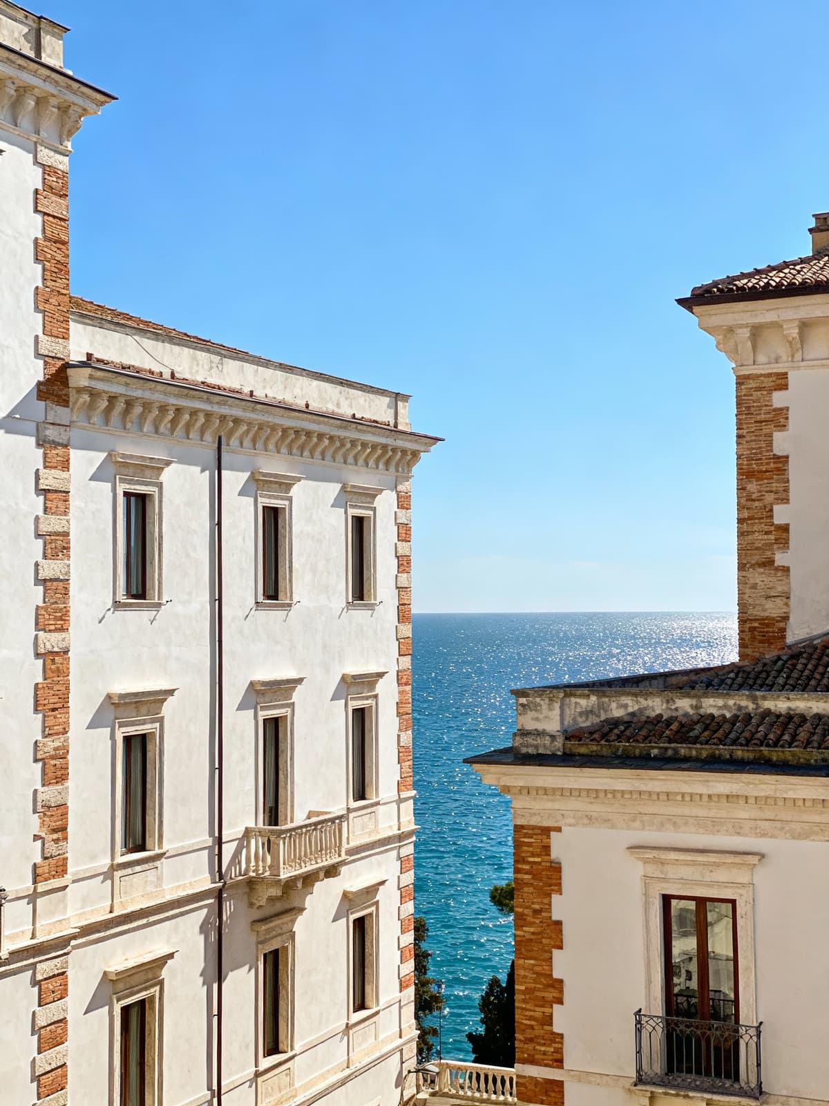 Historic buildings in the heart of Ancona overlooking the Adriatic Sea, showcasing light plaster and brick details under a blue spring sky.